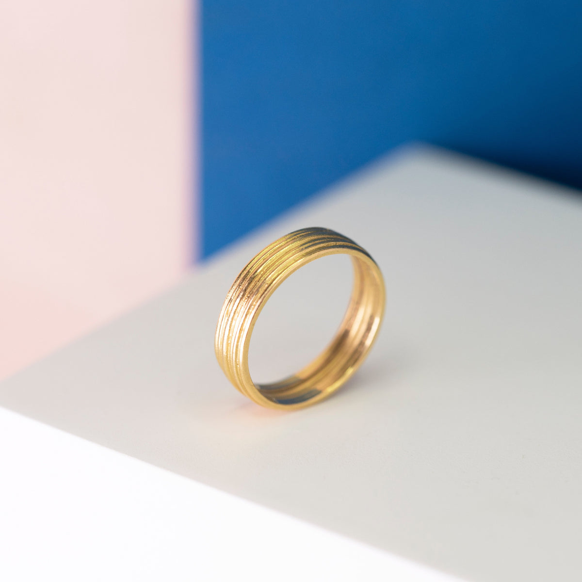 Linear Gold Banded Ring on a coloured background
