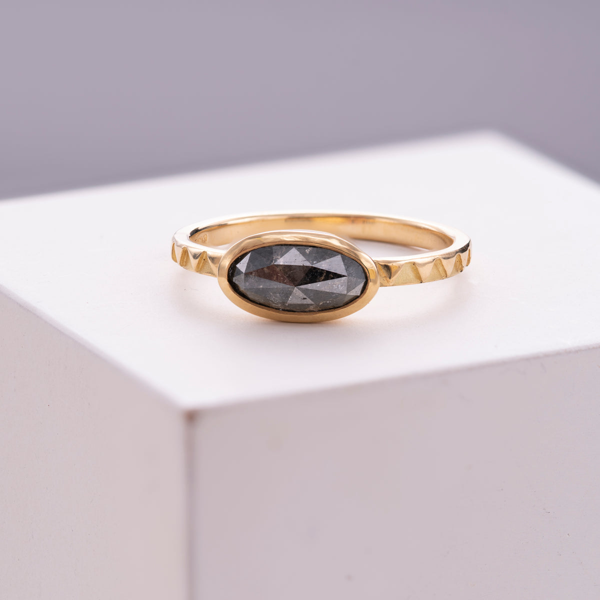 Eclipse 18ct Gold & Grey Oval Diamond Ring, an ellipse rose-cut grey diamond on a triangular-patterned Atlas band, shown on a white background.