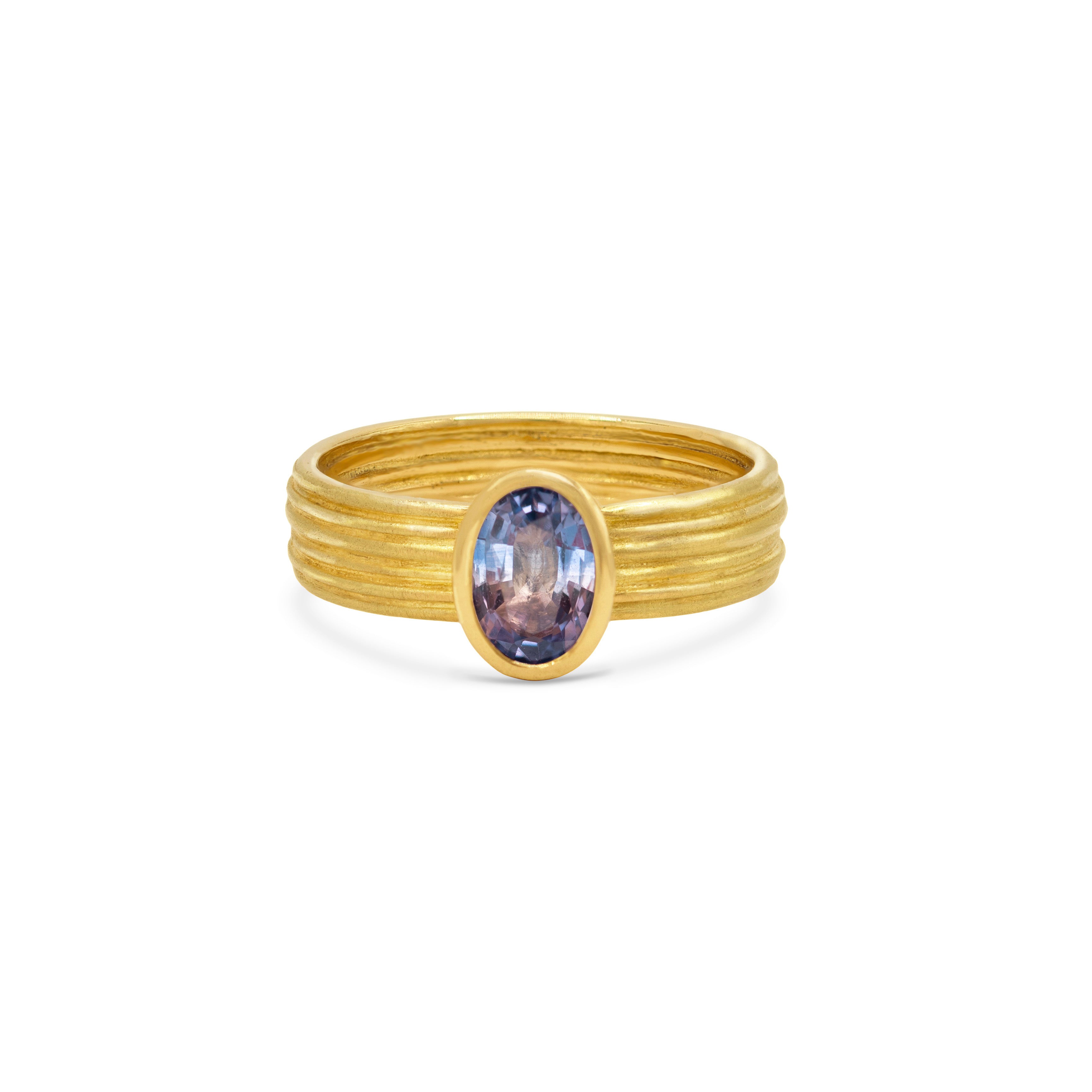 Tri-Colour Sapphire and 18ct Gold Ring, an oval-cut sapphire in violet, blue and clear tones set on a ribbed gold band, shown on a white background.