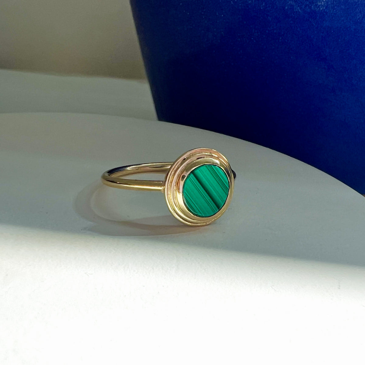 Ascent Gold Ring with Malachite Stone shown at an angle against a styled backdrop.