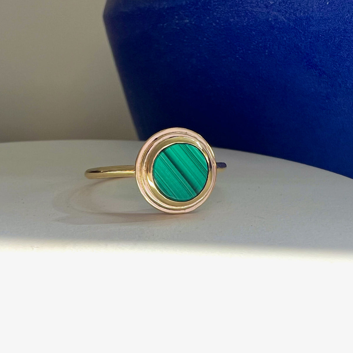 Ascent Gold Ring with Malachite Stone, a round malachite cabochon in a stepped gold frame, shown against a styled backdrop.